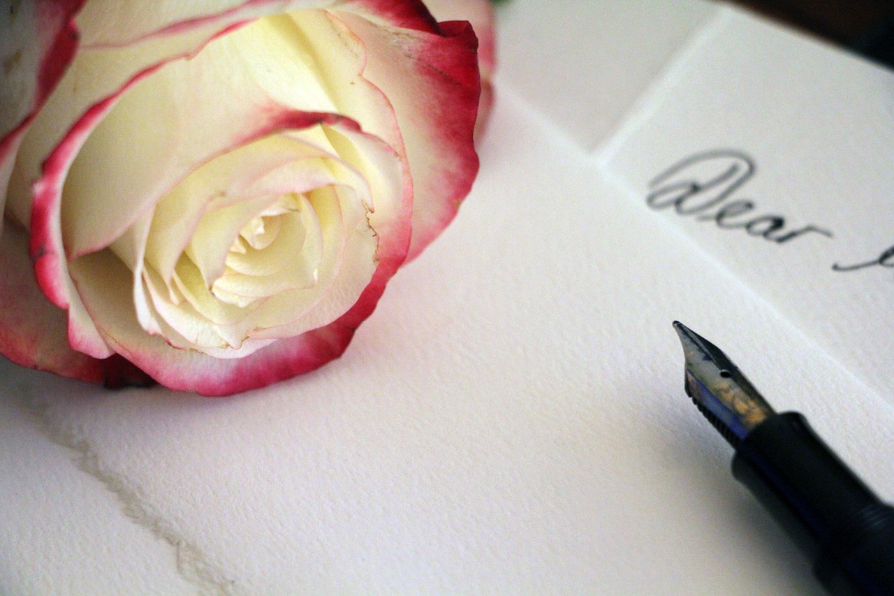 Blank paper, pen, and a pale white and pink rose